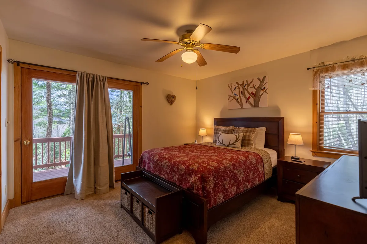 A bright, inviting bedroom with a comfortable bed positioned near large windows that flood the room with natural light. The space features tasteful artwork and a cozy, serene atmosphere, ideal for relaxation and privacy.
