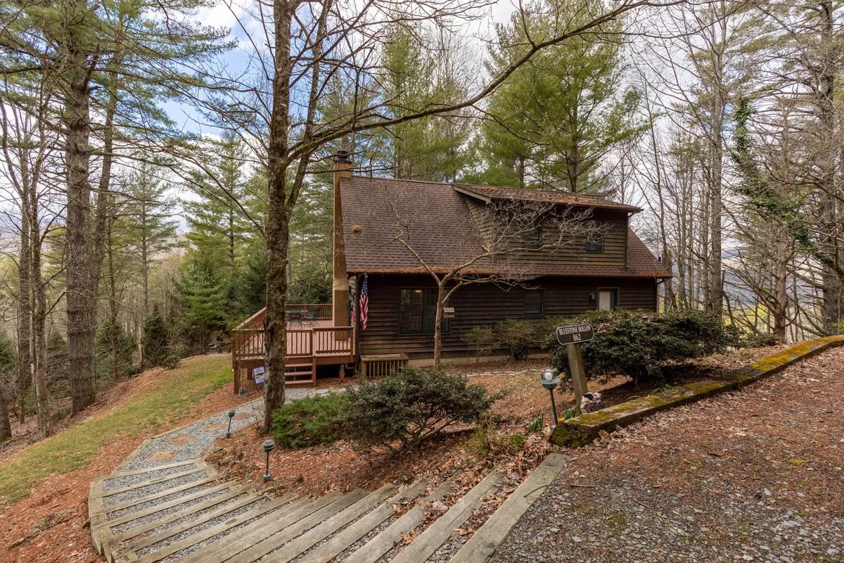 A peaceful scene showing a wooden cabin with a deck and railing, a winding path leading through lush trees, and the warm glow of sunlight filtering through the leaves. The setting suggests privacy and immersion in nature, inviting quiet mornings or scenic strolls.
